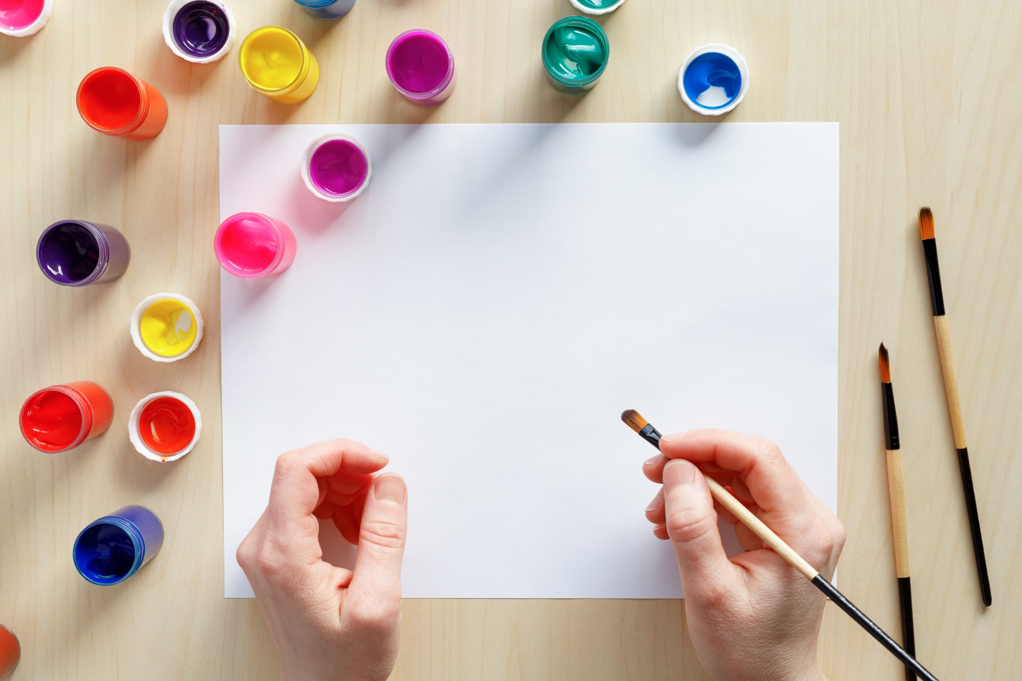 Hands holding paintbrush ready to pain with colored paints on blank paper
